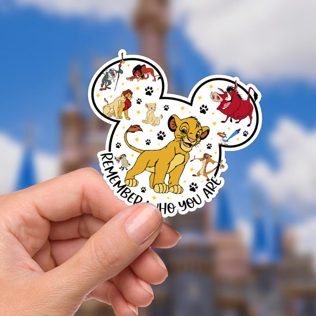 A Disney Lion King themed sticker in the shape of Mickey Mouse ears. The sticker features Simba, Timon, Pumbaa, and other characters. The sticker is yellow, red, and black with the words 'Remember Who You Are'.