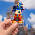 A Mickey Mouse sorcerer sticker in a wizard costume. Mickey wears a blue hat with a crescent moon and star, a red cloak, and blue shorts. The sticker has a holographic, iridescent finish, hydro bottle laptop planner decal sticker.