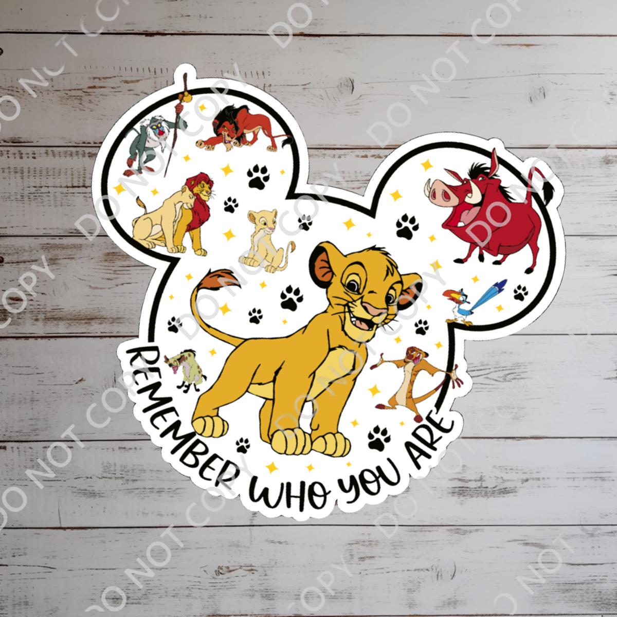 A colorful Lion King themed sticker in the shape of Mickey Mouse ears. The sticker features Simba, Timon, Pumbaa, and other characters. The phrase 'Remember Who You Are' is written in a curved font. Paw prints and stars are scattered around the characters.