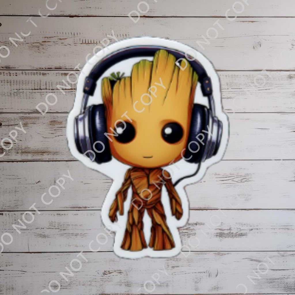 A sticker featuring Baby Groot from Guardians of the Galaxy wearing black headphones. Groot is depicted with a brown, wooden-like body and a smiling face. The background is a blurred image of a blue sky and a castle, suggesting a theme park setting.