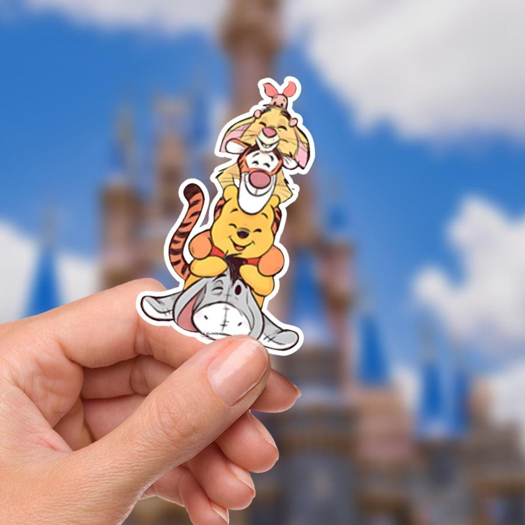 Disney  Winnie The Pooh Disney Laptop Sticker Positive Affirmation planner stationery decal water bottle cell  A colorful sticker featuring Winnie the Pooh characters. Eeyore is at the bottom, supporting Winnie the Pooh, who is supporting Tigger, who is supporting Piglet. The sticker is held by a hand in front of a blurred background of a blue sky and a castle.